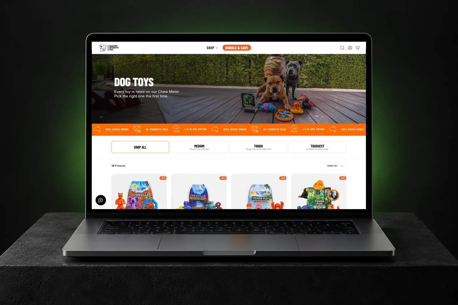 Happy Staffy Co Shopify store on a laptop, showing the Dog toys collection with Staffies on a deck, chew rating tabs and toy cards | EVDEV
